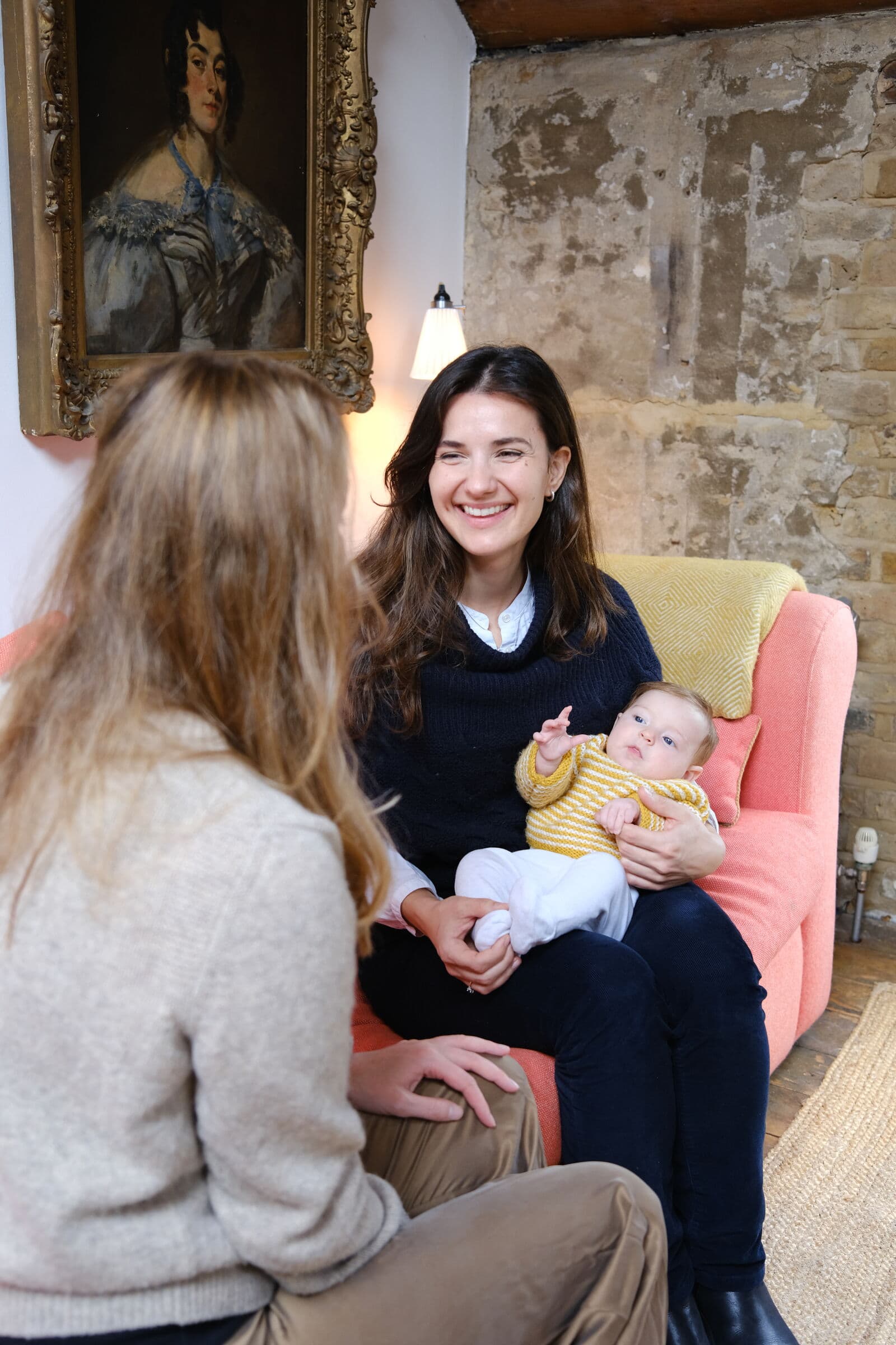 Midwife smiling at a mother while holding her baby on the sofa