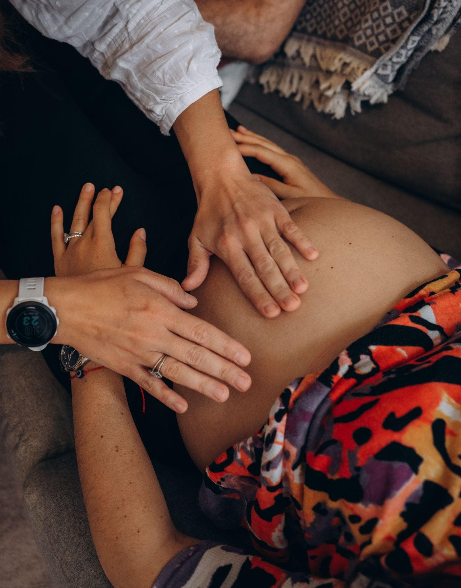 A midwife's hands on a pregnant woman's bump, the mother's hands beside them