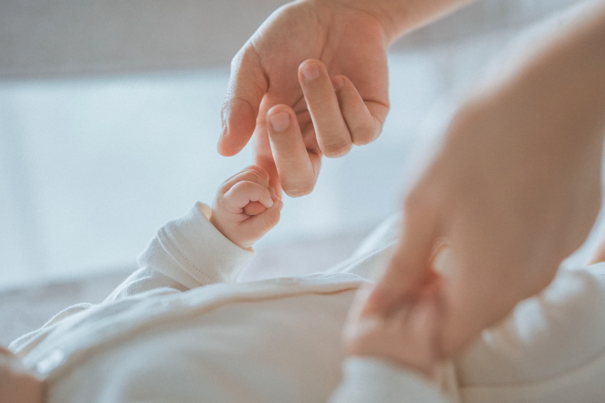 A newborn's hand gripping an adult's finger